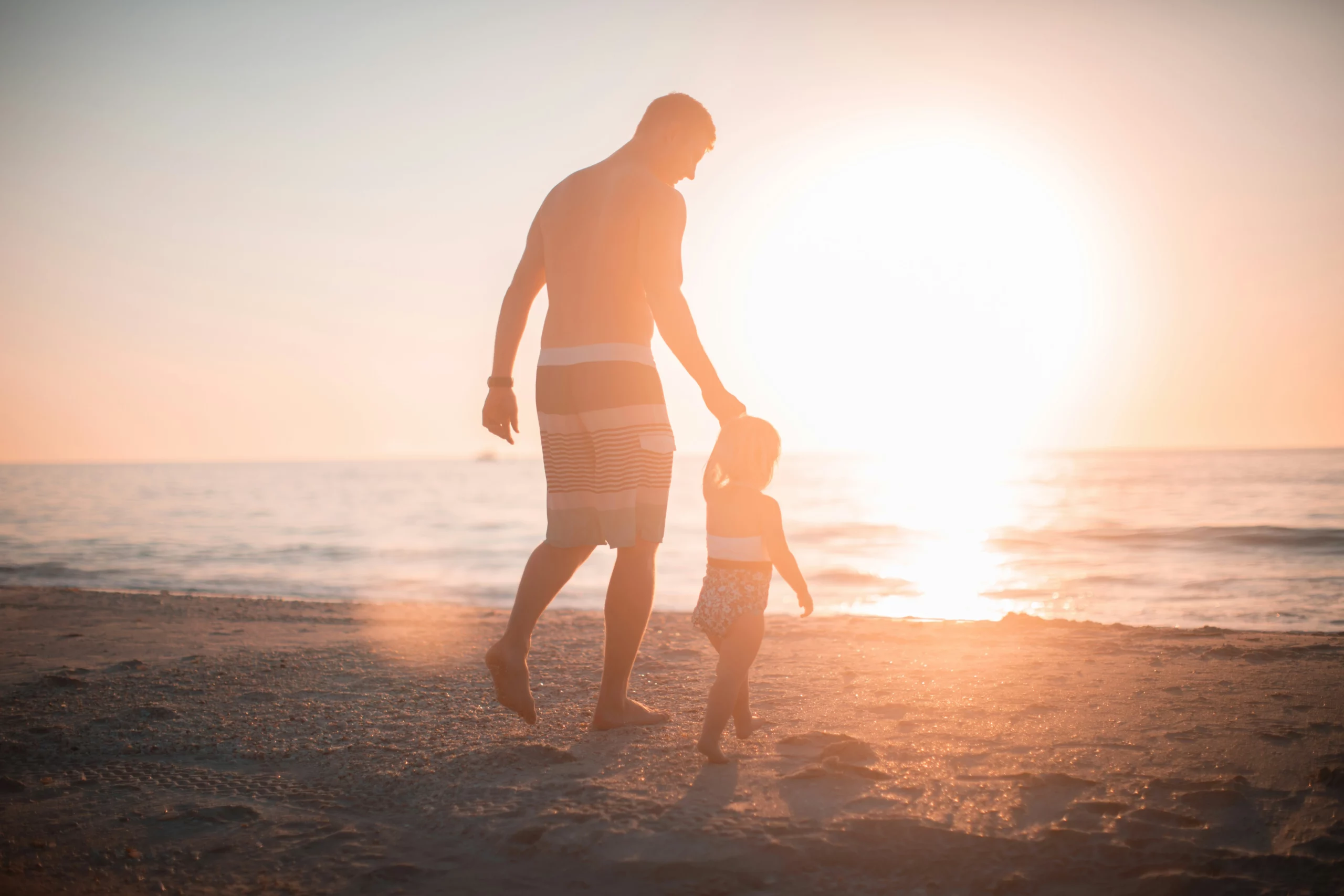 image d'un père et son enfant au bord de la mer face à un coucher de soleil pour symboliser le deuil d'un papa, d'un père